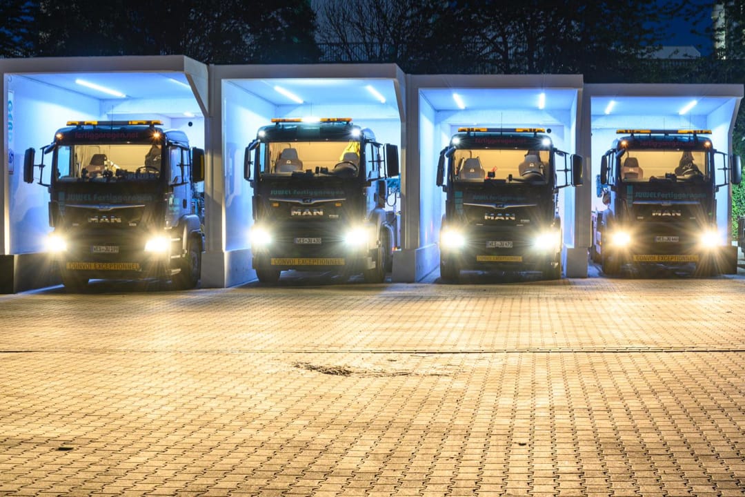 Schlüsselfertige JUWEL-Fertiggaragen bei Nacht, vier beleuchtete Garagen mit geparkten MAN-Lkw, zeigt die schnelle und unkomplizierte Installation von Betonfertiggaragen.